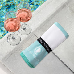 The Coastline Beach Towel rolled up in aqua and white, showcasing its soft and absorbent fabric, perfect for summer.